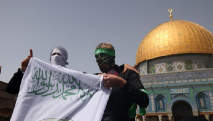 Pria bertopeng angkat spanduk Brigade Ezzedine al-Qassam setelah shalat Jumat pertama di bulan puasa Ramadhan, di depan Dome of the Rock di Masjidil Haram, Yerusalem, pada 24 Maret 2023.